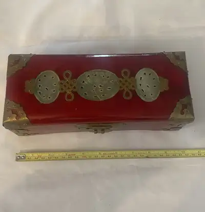 This is an antique box, featuring a red lacquer finish adorned with brass accents and jade ornaments...