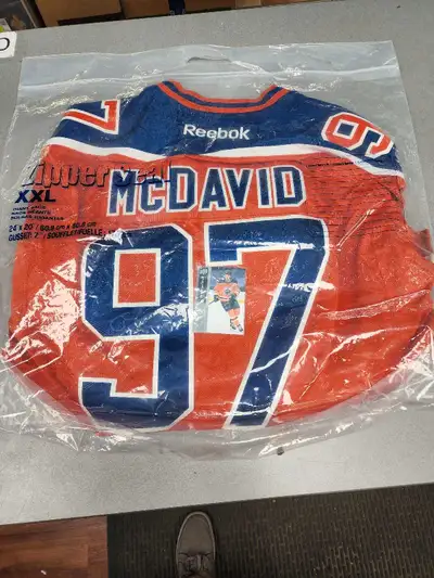 Here I have a Connor McDavid jersey and trading card. The jersey is orange and blue, featuring the n...