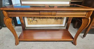 Wooden hall table has a medium brown finish with two glass top inserts. The apron features a fluted...