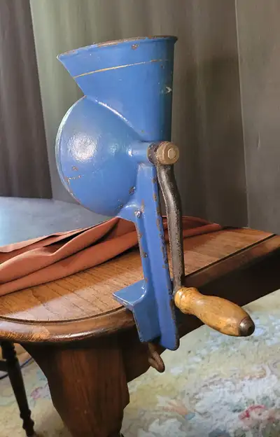 Antique cast metal portable manual slicer mincer. Blue with a silver stripe around the hopper. Handl...