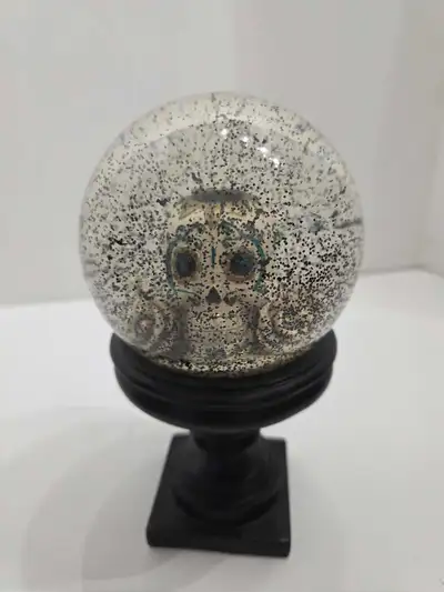 This used Day of the Dead snow globe features a sugar skull design inside a clear glass globe, fille...