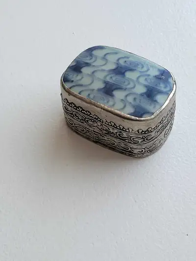 This vintage trinket box features a blue and white patterned ceramic top set in a decorative silver...