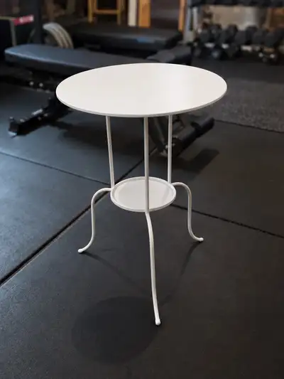 Selling a round white-coloured accent table with a white metal frame and a small lower shelf. Featur...