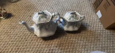 This elegant vintage porcelain teapot and matching sugar bowl set features a delicate blue floral pa...