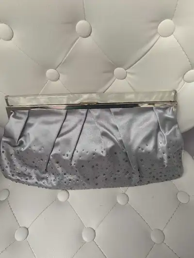Silver satin clutch with a silver chain and a pearlescent clasp. The clutch is embellished with rhin...