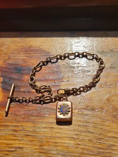 Vintage pocket watch chain has a square fob locket. Fob charm features an enameled emblem with a cro...