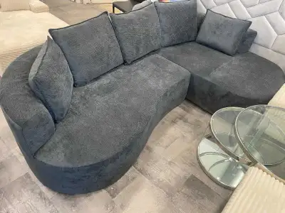 This modern curved sectional features smooth dark‑grey upholstery, plush back cushions, and a contem...