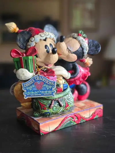 This charming Disney Traditions Jim Shore figurine captures a festive scene of Mickey and Minnie sha...