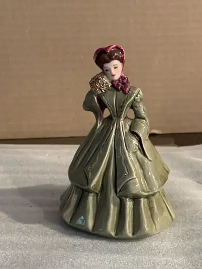 This pre-owned Romance Creations porcelain figurine features a woman in an elegant olive green dress...