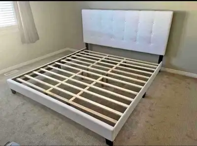 This queen-size bed frame features a stylish white upholstered headboard and a sturdy wooden slat su...
