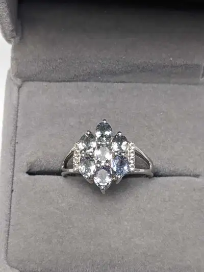Brand new rhodium plated ring featuring a floral cluster of oval cut tanzanite accented by round whi...