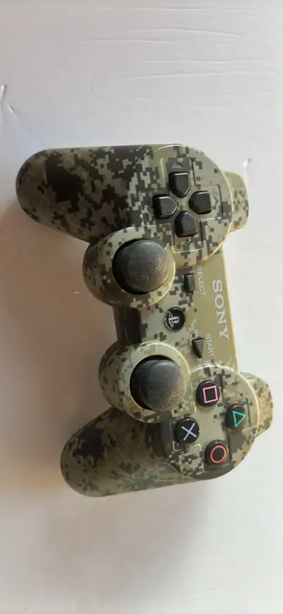 This is a pre-owned Sony DualShock 3 wireless controller, featuring a unique urban camouflage patter...