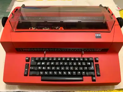 Manufactured in 1973, this correcting typewriter is coral red in colour and has 4 spare typing eleme...