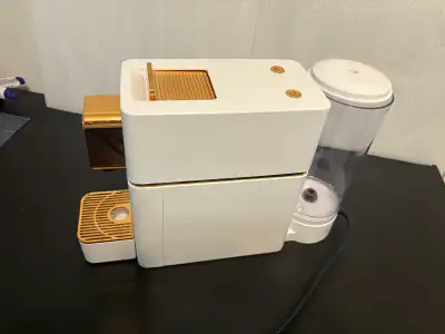 Cette machine à espresso Nespresso élégante, de couleur blanche avec des finitions dorées, neuve et...