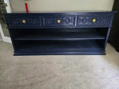 Navy blue console table is constructed from wood with two drawers containing ornate carved patterns...