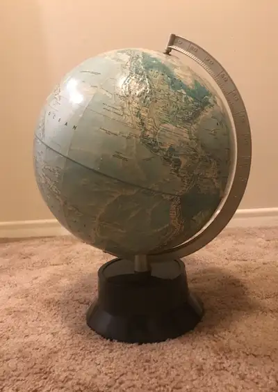 Offering a vintage 12” blue topographical World globe on stand made by Rand McNally in the 1980s. Th...