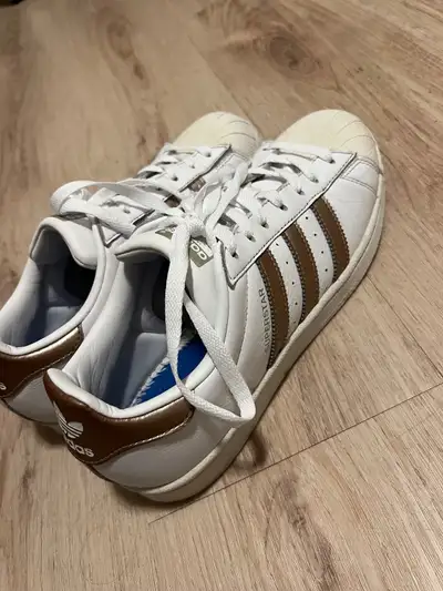 Women's Adidas Superstar sneakers. White leather upper with rose gold stripes. Classic design, comfo...