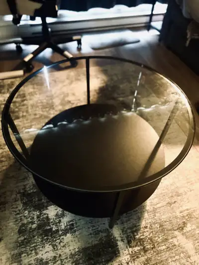 Modern round coffee table has a tempered glass top and a black metal frame. This IKEA VITTSJÖ model...
