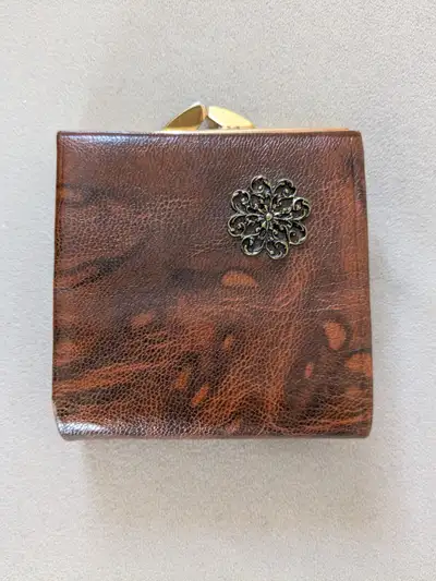Cognac colored goatskin leather bifold wallet. Floral emblem with gold kiss lock clasp. Features ful...
