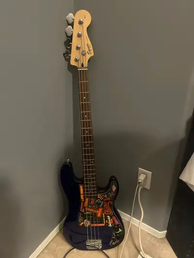 This Squier Jazz Bass is a pre-owned instrument featuring a sleek blue finish adorned with a unique...