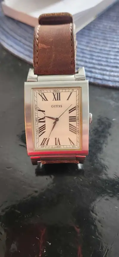 This is a used Guess tank watch featuring a Nixon leather strap. The watch has a cream-colored face...