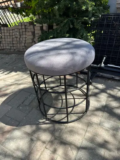 Round grey fabric seat. Black metal frame. Good for extra seating or a side table.