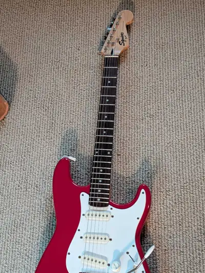 This Squier Stratocaster electric guitar features a vibrant red finish, a maple neck with a smooth r...