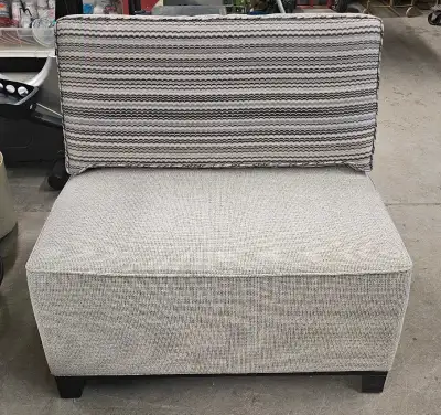 Stylish armless chair. Has a neutral gray textured fabric on main body. Back cushion is striped with...