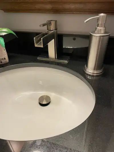 This Pfister vanity faucet features a sleek, modern waterfall design with a brushed nickel finish, a...