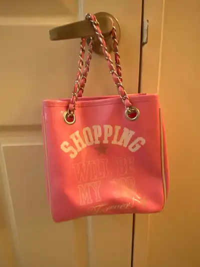 Pink tote bag with chain strap. Features a white slogan on the front that says 'Shopping will be my...