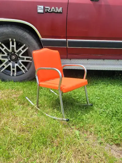 This is a groovy vintage kids rocking chair with a vibrant orange seat and a sleek chrome frame, per...