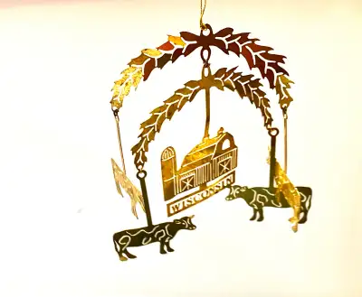 Intricate gold-toned metal ornament has a hanging design with a central barn and silo above the word...