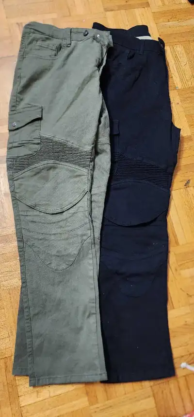 Two pairs of men's cargo pants. One pair is green and the other pair is black. They have knee pads a...