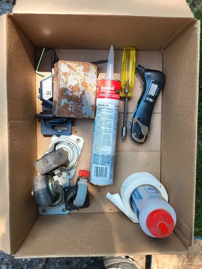 A collection of tools in a cardboard box. Includes caulk, a screwdriver, and more. Consider how grea...