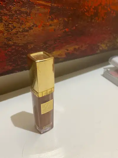 Lip gloss in a gold tube. The lip gloss colour is a golden brown.