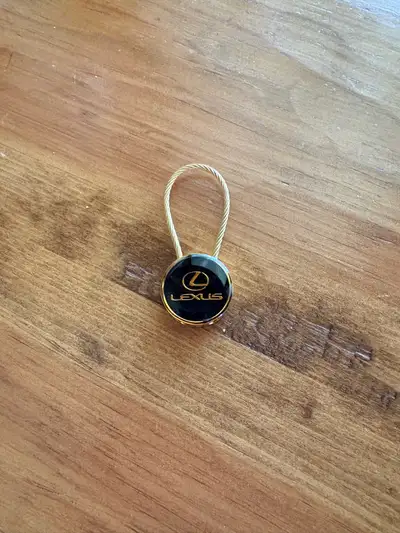 This Lexus key chain features the brand's logo in gold against a black background, attached to a dur...