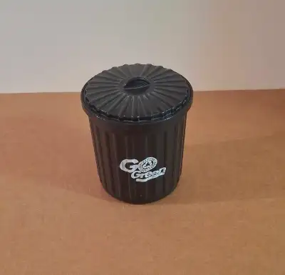 A small, black, lightly used plastic recycling/storage container with a lid that looks like a garbag...