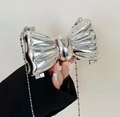 Add a touch of whimsy to your wardrobe with this eye-catching silver bow purse featuring a delicate...