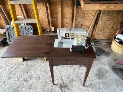 Singer sewing machine comes built into a brown wood-grain laminate cabinet. The cabinet has a fold-o...