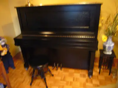 PIANO DROIT EN CHÈNE, LAQUÉ NOIR, SUR ROULETTES AVEC BANC ROND PIVOTANT, HAUTEUR AJUSTABLE. COMME NE...