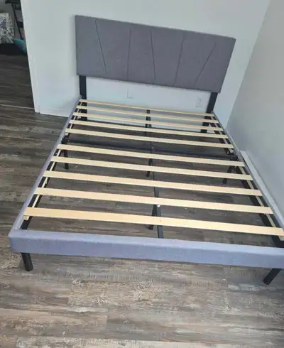 This double bed frame features a modern grey upholstered headboard and sturdy wooden slats, providin...