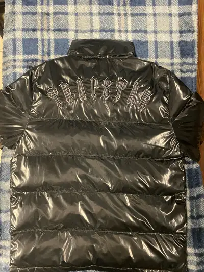 This is a stylish, used black Trapstar puffer jacket, perfect for staying warm and making a statemen...