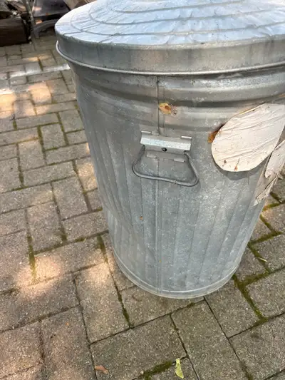 This is a used metal garbage can, perfect for outdoor use. It has some signs of wear, which only add...