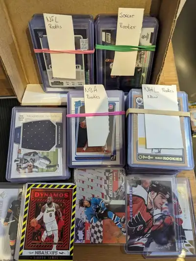 Over 150 rookie cards (NHL NBA NFL EPL) including autographed & numbered cards Plus de 150 cartes de...